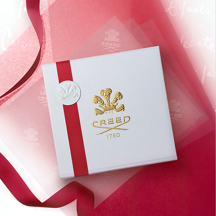 White box with red ribbon and Creed logo on a pink background