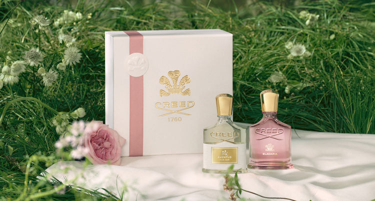Two Creed perfume bottles with a white box on a grassy background
