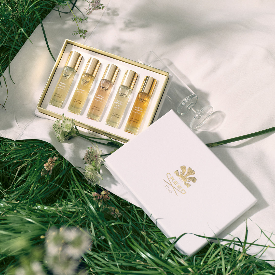 Set of skincare bottles in a gold box on a white surface with green grass and flowers.