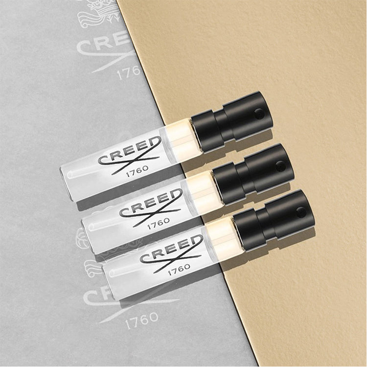 Three Creed perfume bottles on a gray and beige background